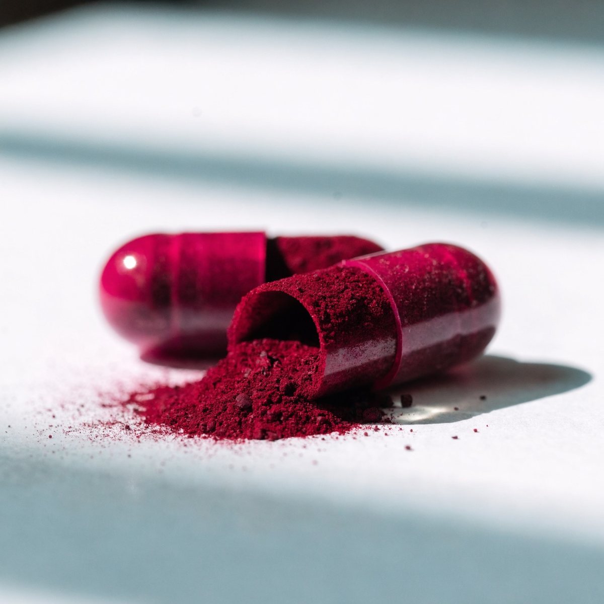 Close-up of two capsules, one opened to show the beetroot powder.